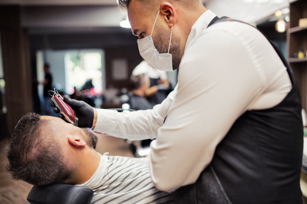 Handsome hipster man client visiting haidresser and hairstylist in barber shop.