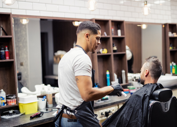 Rear view shot of man client visiting haidresser and hairstylist in barber shop.