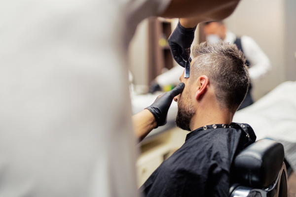 A hipster man client visiting haidresser and hairstylist in barber shop.