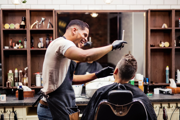 Rear view shot of man client visiting haidresser and hairstylist in barber shop.