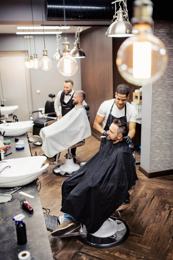 A high angle view of man clients visiting haidresser and hairstylist in barber shop.