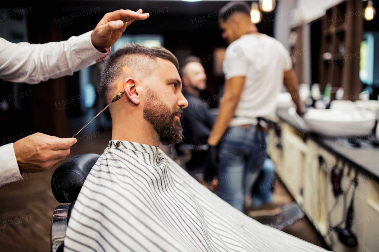 Handsome hipster man client visiting haidresser and hairstylist in barber shop, ear hair removal.