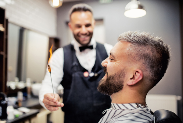 Handsome hipster man client visiting haidresser and hairstylist in barber shop, ear hair removal.