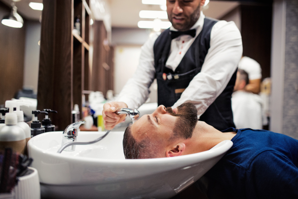 Handsome hipster man client visiting haidresser and hairstylist in barber shop.