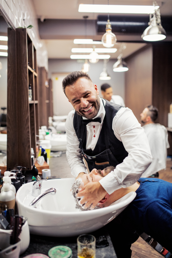 Handsome hipster man client visiting haidresser and hairstylist in barber shop.