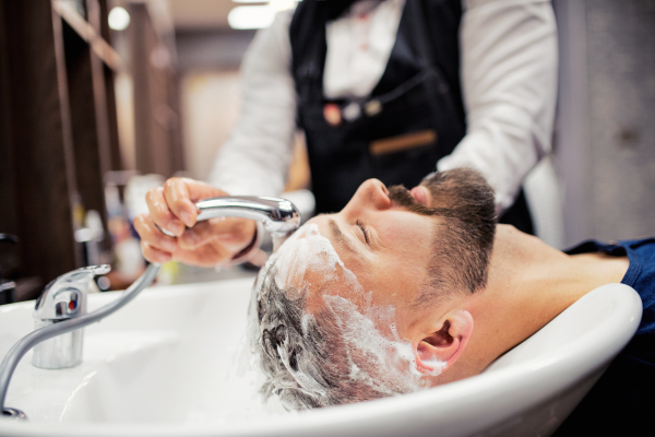 Handsome hipster man client visiting haidresser and hairstylist in barber shop.