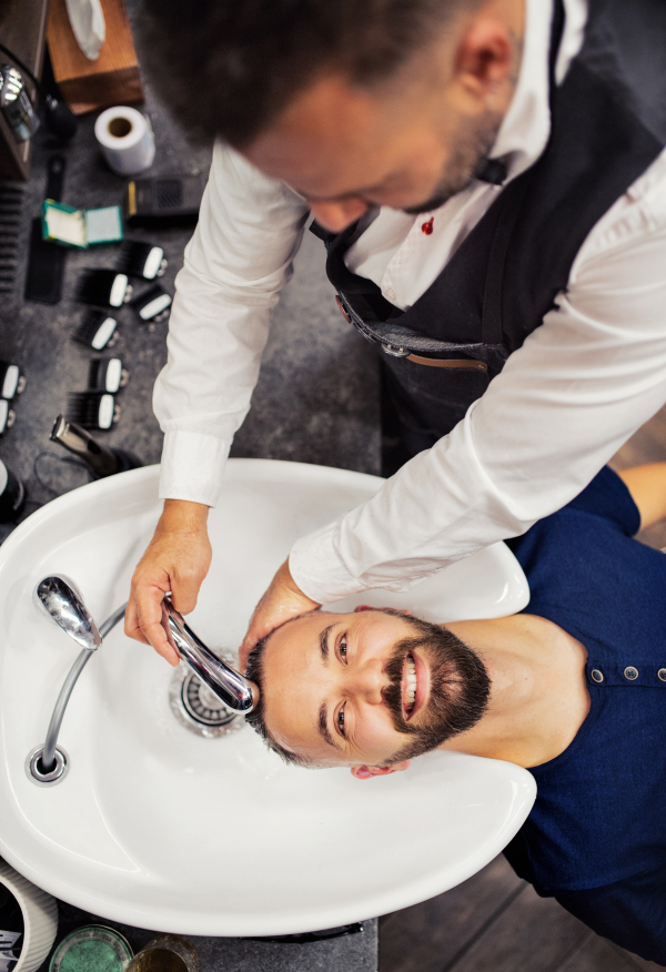 A top view of handsome hipster man client visiting haidresser and hairstylist in barber shop.