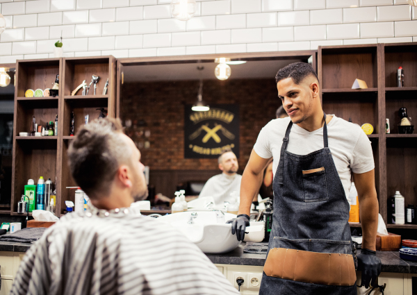 A mature man client talking to haidresser and hairstylist in barber shop.