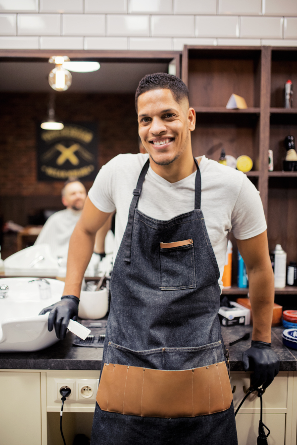 Young handsome hispanic haidresser and hairstylist standing in barber shop.