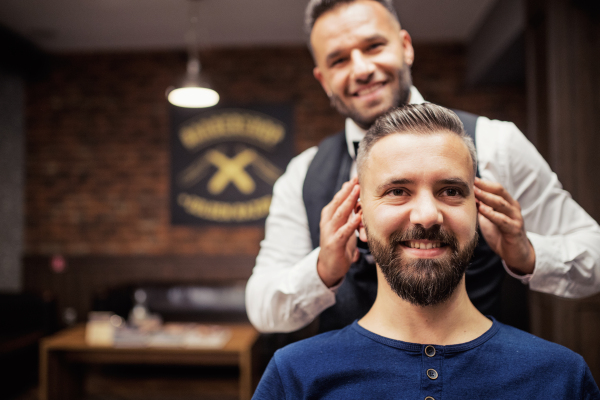 Handsome hipster man client visiting haidresser and hairstylist in barber shop. Copy space.