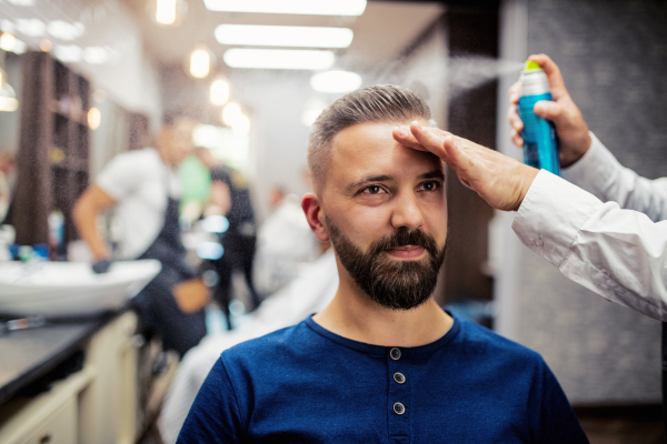 Handsome hipster man client visiting haidresser and hairstylist in barber shop.