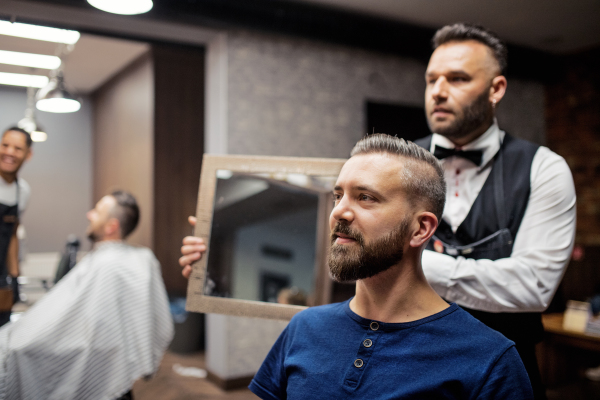 Handsome hipster man client visiting haidresser and hairstylist in barber shop.