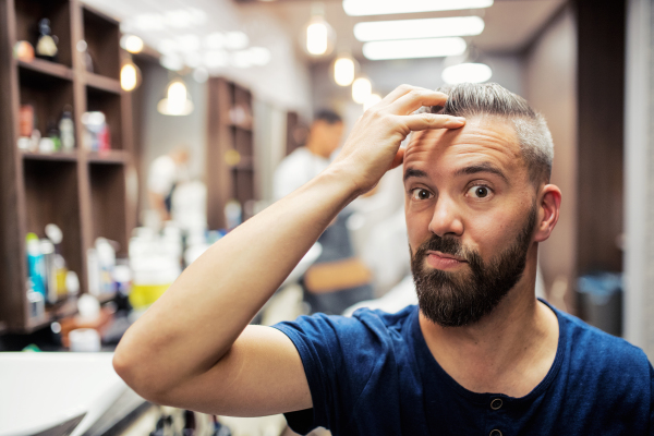 Handsome hipster man client visiting haidresser and hairstylist in barber shop.