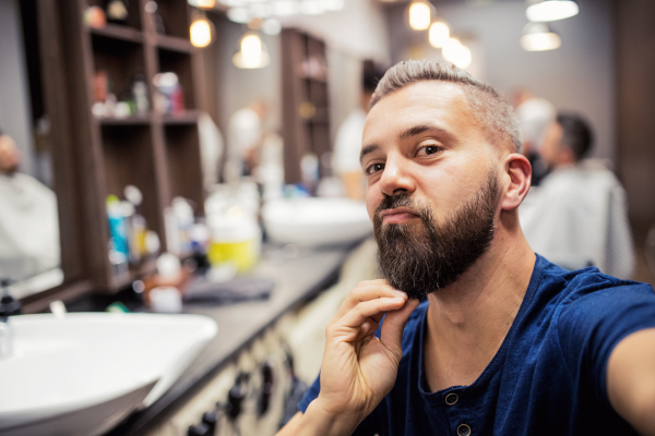 Handsome hipster man client visiting haidresser and hairstylist in barber shop, making funny faces.