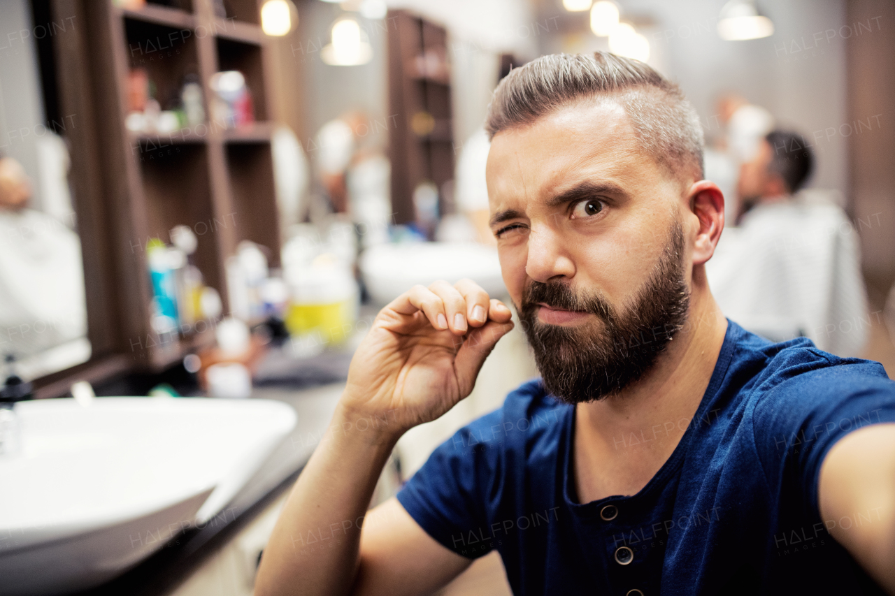 A hipster man client in barber shop, winking when taking seflie.