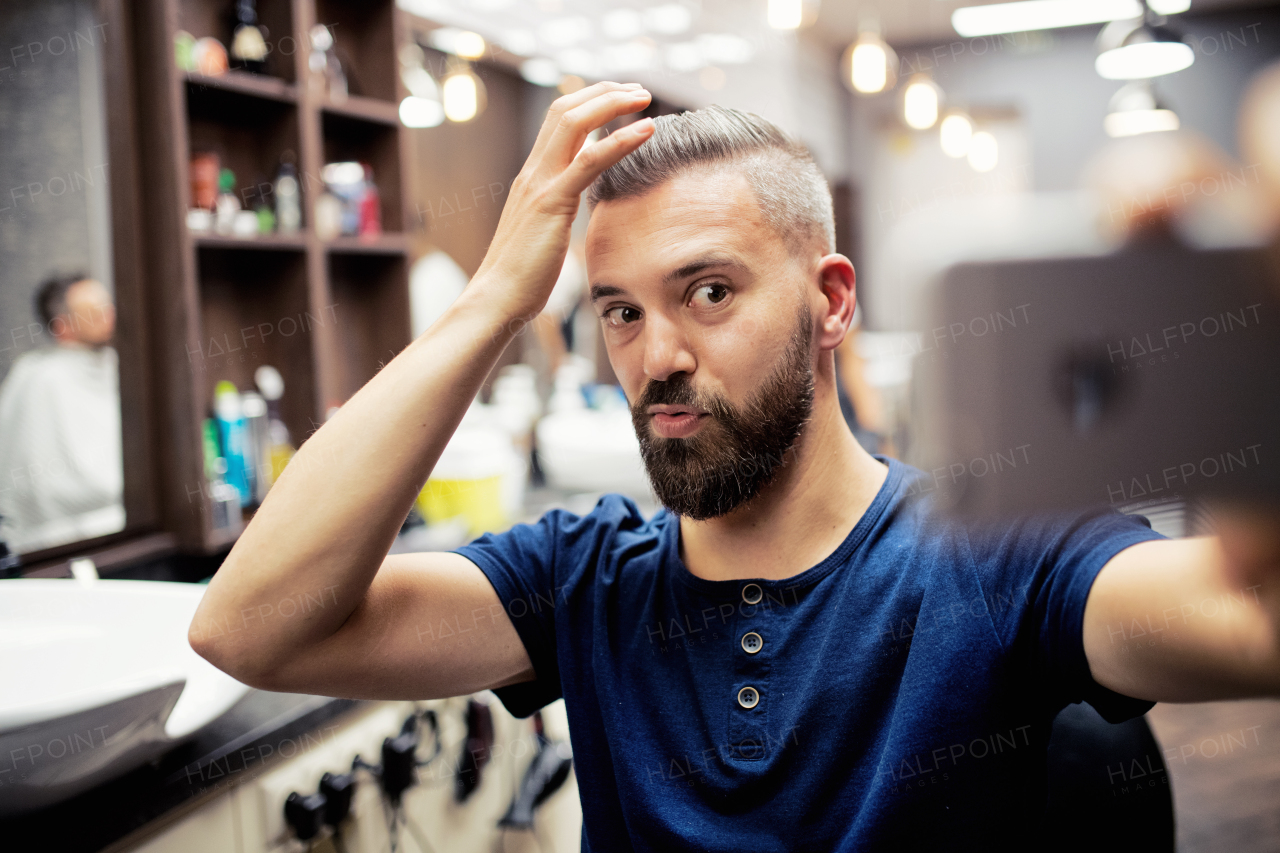 A hipster man client in barber shop, making funny faces when taking seflie.