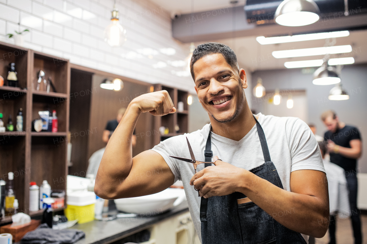 Young handsome hispanic haidresser and hairstylist standing in barber shop, flexing muscles.