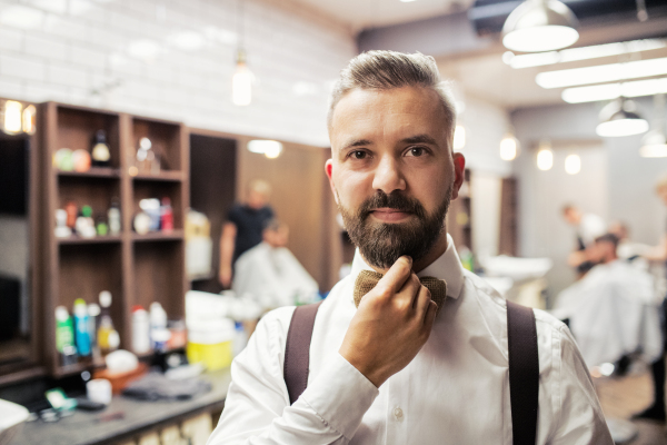 A portrait of handsome hipster man client standing in barber shop. Copy space.