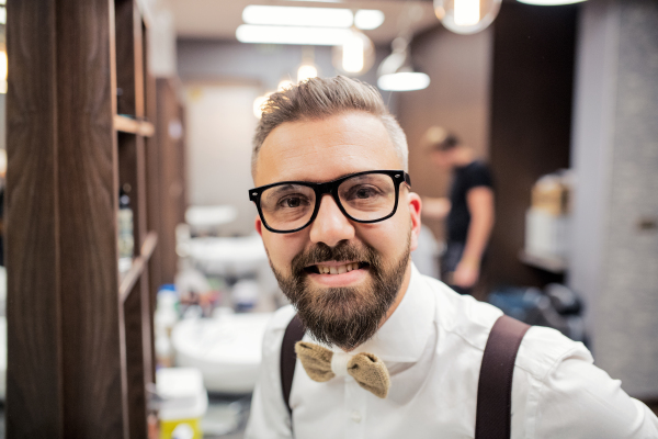 A portrait of handsome hipster man client standing in barber shop. Copy space.