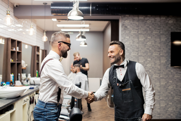 Handsome hipster man client shaking hands with haidresser and hairstylist in barber shop.