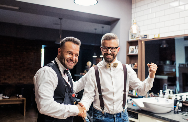 Handsome hipster man client shaking hands with haidresser and hairstylist in barber shop.