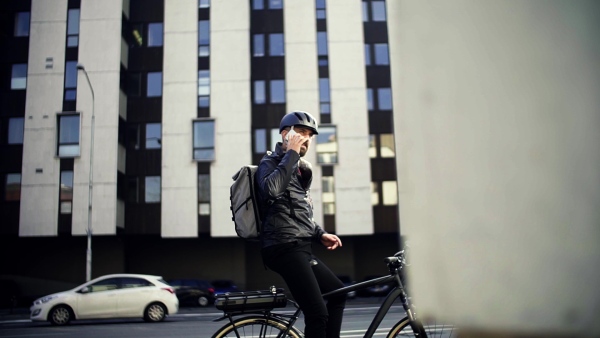 A portrait of male bicycle courier with backpack delivering packages in city, using smartphone. Slow motion.