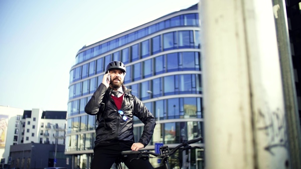 A businessman commuter with bicycle going home from work in city, using smartphone. Slow motion.