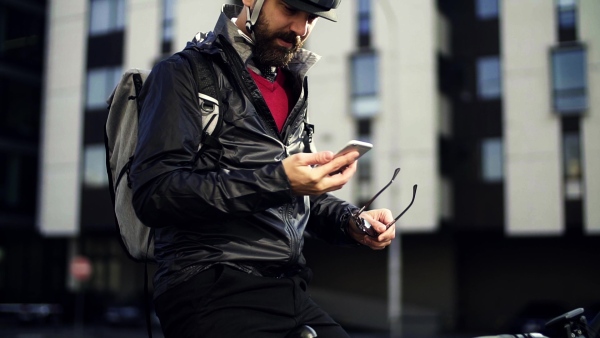 A businessman commuter with bicycle going home from work in city, using smartphone. Slow motion.