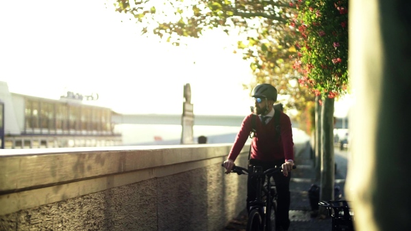 A hipster businessman commuter with electric bicycle traveling to or from work in city. Slow motion.