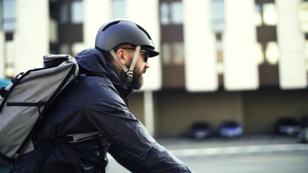 Male hipster courier with bicycle cycling along road in city, delivering packages. Slow motion.