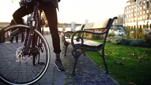 Hipster businessman commuter with helmet sitting down on a bench when traveling home from work in city. Slow motion.