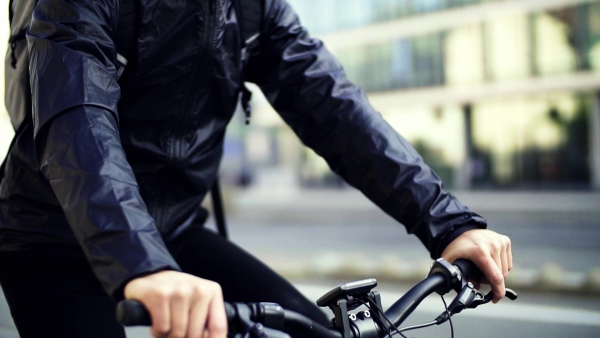 Male hipster courier with bicycle cycling along road in city, delivering packages. Slow motion.