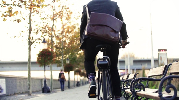 A rear view of businessman commuter with electric bicycle traveling to or from work in city. Slow motion.