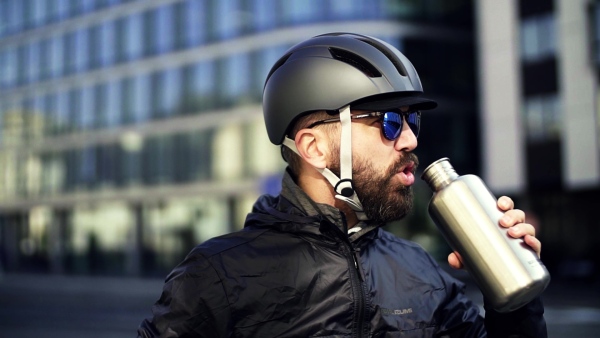 Male courier with sunglasses drinking water when delivering packages in city. Slow motion.