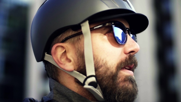 An extreme close-up of a male cyclist with bicycle helmet and sunglasses in city, drinking from a steel bottle. Slow motion.