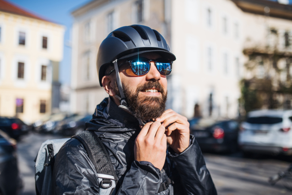 Male hipster courier putting on a helmet in city, delivering packages. Copy space.