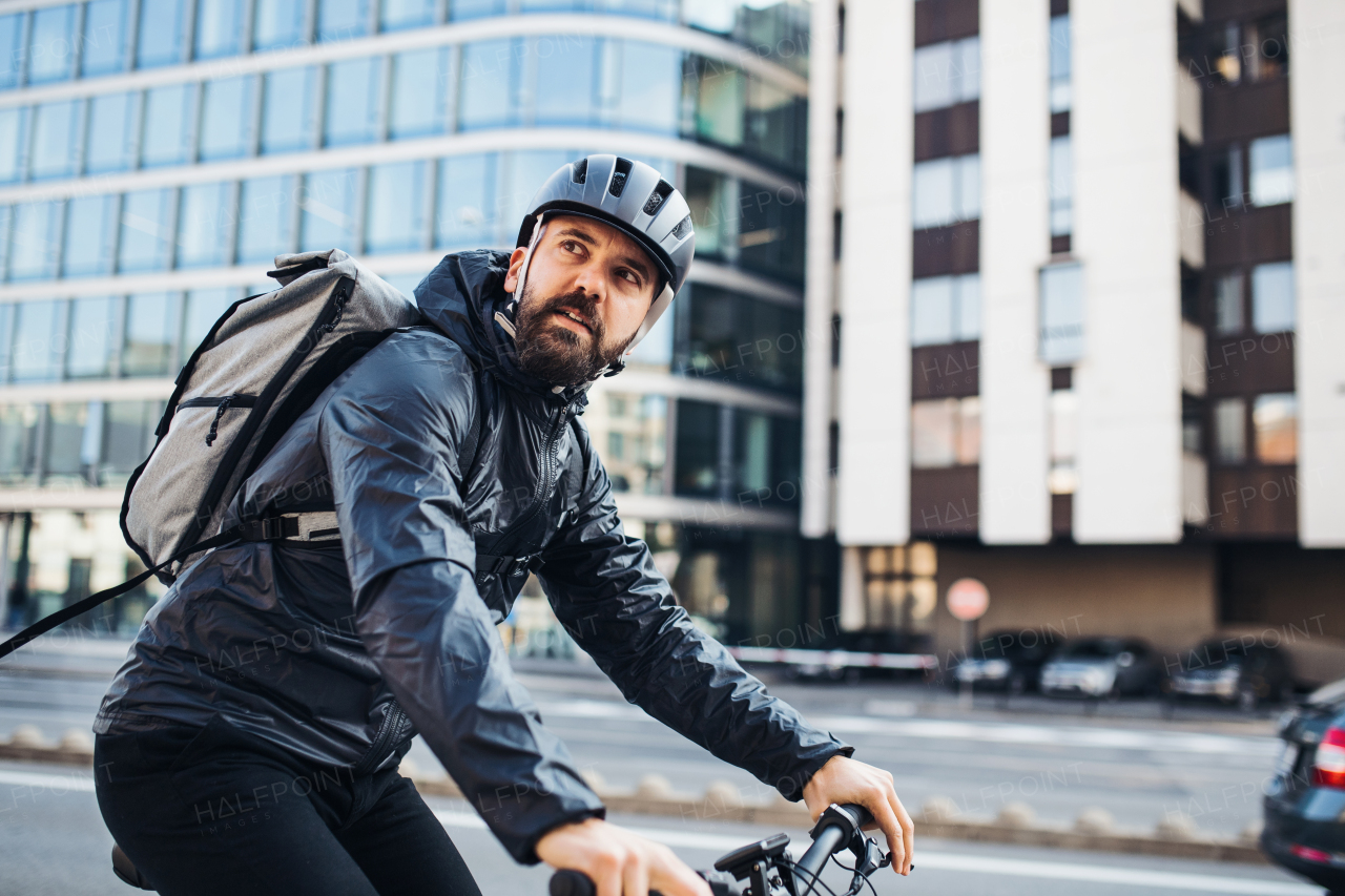 Male hipster courier with bicycle cycling on a road in city, delivering packages. Copy space.