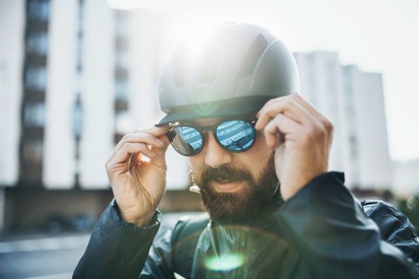 Male hipster bicycle courier with helmet putting on sunglasses in city when delivering packages.