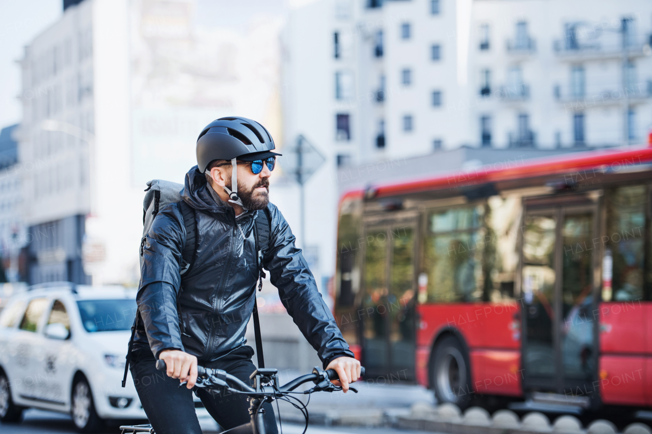 Male hipster courier with bicycle cycling on a busy road in city, delivering packages. Copy space.