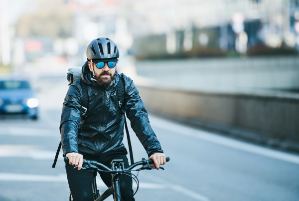 A front view of male bicycle courier with sunglasses cycling in city, delivering packages. Copy space.