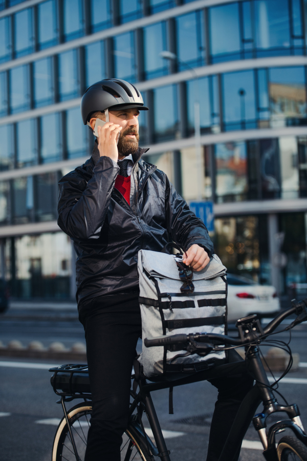 Male hipster courier with bicycle standing on a road in city, making a phone call when delivering packages.