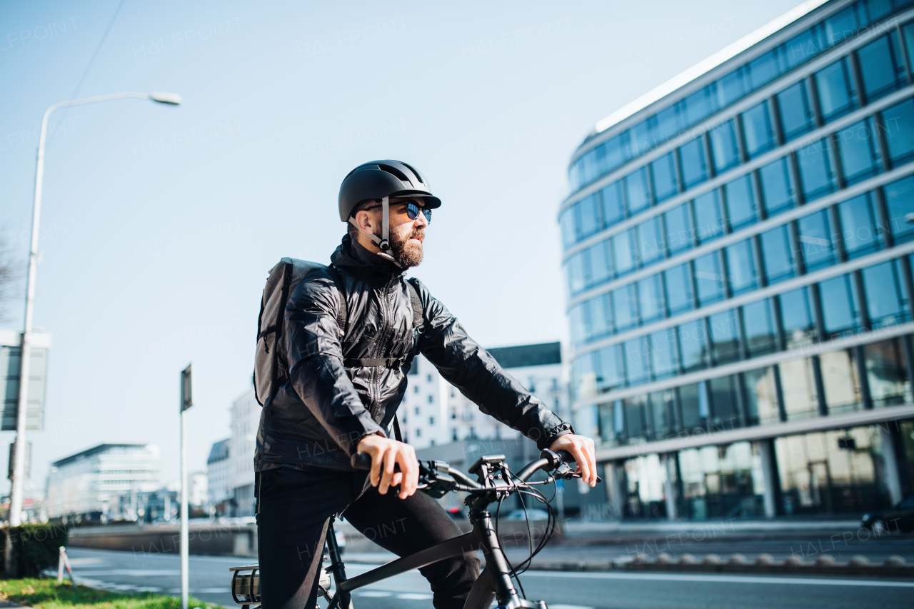 Male hipster courier with bicycle cycling on a road in city, delivering packages. Copy space.