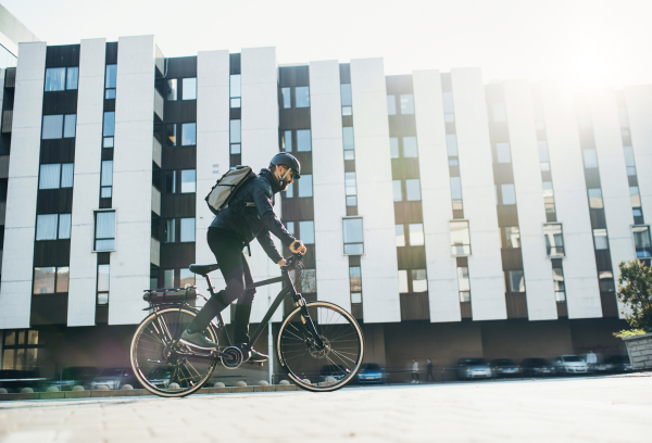 Male hipster courier with bicycle cycling on a road in city, delivering packages. Copy space.