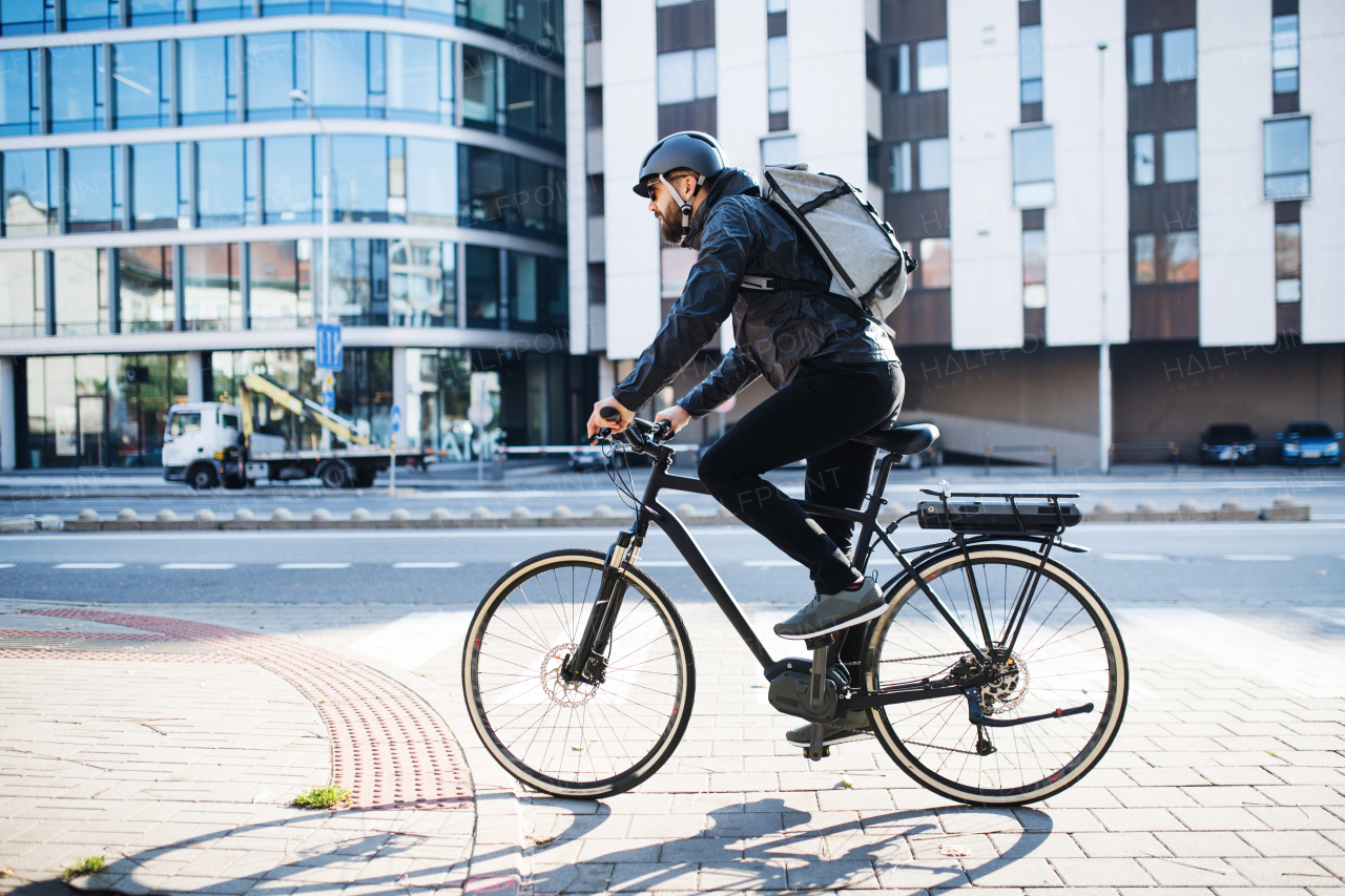 Male hipster courier with bicycle cycling on a road in city, delivering packages. Copy space.