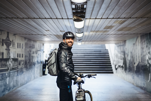 Male bicycle courier standing in subway when delivering packages in city. Copy space.