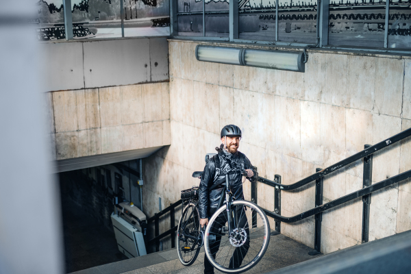 Male courier delivering packages in city, carrying bicycle up the stairs. Copy space.