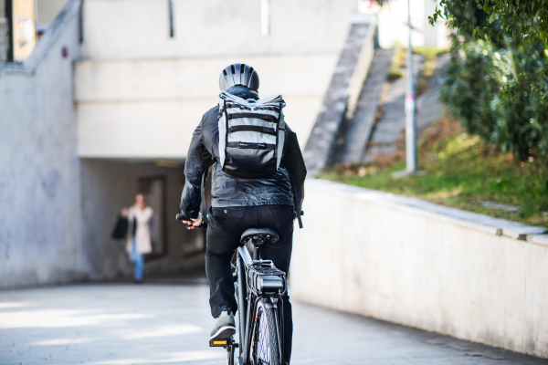 A rear view of male bicycle courier cycling in city, delivering packages. Copy space.