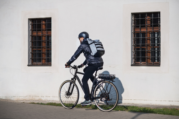 A rear view of a courier with bicycle cycling in city, delivering packages.