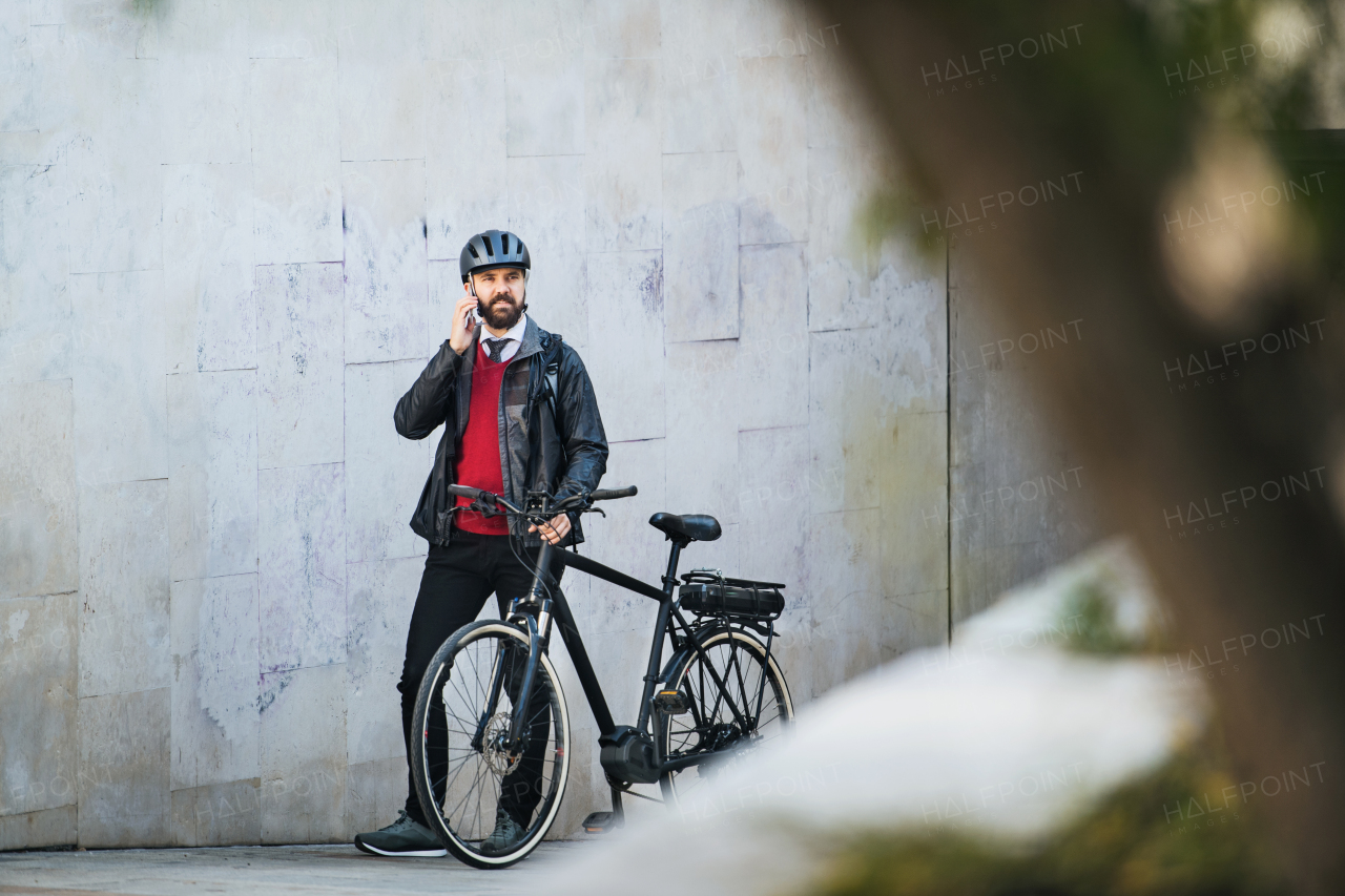 A businessman commuter with bicycle walking home from work in city, using smartphone.