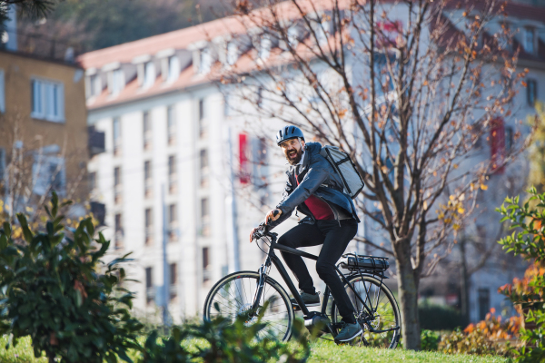 Male hipster courier with electric bicycle delivering packages in city.